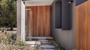 A modern outdoor shower area with a wooden panel wall, a concrete pathway, and a security camera. - ESCAPE TO PICTURESQUE EAGLE BAY IN THIS BEAUTIFULLY APPOINTED 2 BED STUDIO (Eagle Bay)