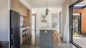 A modern kitchen with a black refrigerator, wooden cabinets, and a central island with stools. - ESCAPE TO PICTURESQUE EAGLE BAY IN THIS BEAUTIFULLY APPOINTED 2 BED STUDIO (Eagle Bay)