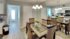Une cuisine moderne avec un coin repas, comprenant une table à plateau en verre, des chaises en osier et un éclairage suspendu.