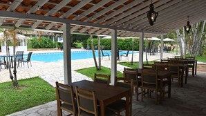 An outdoor patio with stone flooring, wooden tables and chairs, and a pool in the background. - Quinta das Águas by Summit Hotels (Itapira)