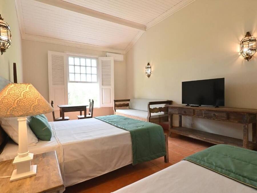 A hotel room with two beds, a TV, a lamp, and a window with shutters.