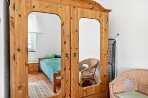 Un armari de fusta amb portes de mirall, un llit amb roba de llit verda, una cadira de vimet i una petita taula de nit.