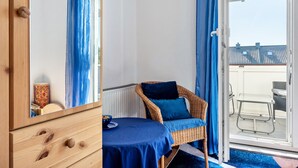 Una habitación con una cama, una silla de mimbre con cojín, una mesita con un cuenco y vistas al exterior.