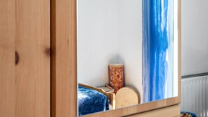 Un armario de madera con un espejo que refleja un rincón de la habitación, un tambor y una cama con una manta azul.