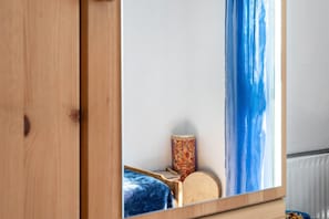 Une armoire en bois avec un miroir qui reflète un coin de la pièce, une batterie et un lit recouvert d’une couverture bleue.