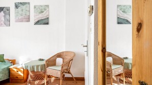 Una habitación con una cama, dos sillas de mimbre, una mesa y tres obras de arte colgadas en la pared.