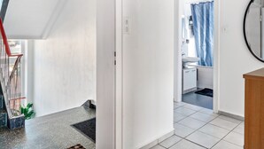 Un pasillo con una escalera, un baño con cortina de ducha y un espejo redondo.