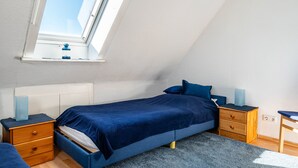 Ein Schlafzimmer mit Oberlicht, einem Bett mit blauer Bettwäsche, einem Nachttisch und einem Schreibtisch.