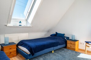 Une chambre avec un puits de lumière, un lit avec une literie bleue, une table de chevet et un bureau.