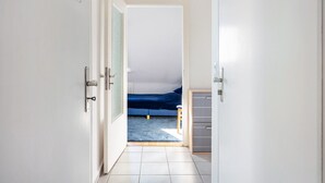 Ein Flur, der zu einem Schlafzimmer mit einem Bett, einem kleinen Hocker und einem Kleiderschrank führt.