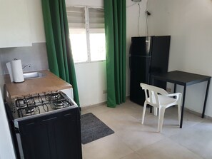 A compact kitchen with a gas stove, a sink, a refrigerator, and a small dining table with a chair.