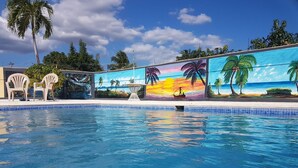 En swimmingpool med en väggmålning som föreställer en solnedgång och palmer.