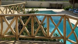 Zwembad met uitzicht op de oceaan, een houten terras en een constructie met rieten dak.