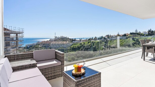 En balkon med havudsigt og bybillede, møbleret med en sofa og et bord med frugt.