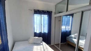 A bedroom with a single bed, a sliding glass door, and a ceiling-mounted smoke detector.