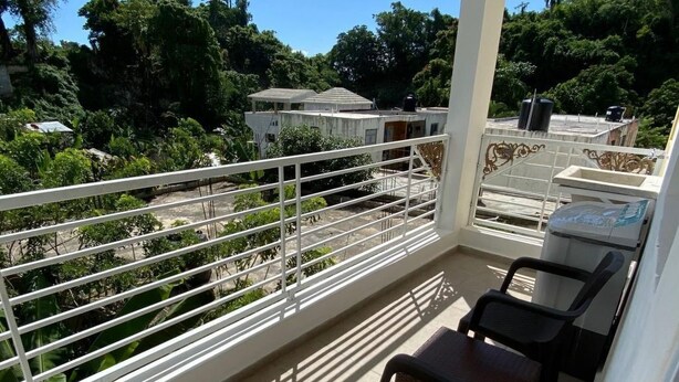 A balcony with a white railing, two black chairs, and a view of a residential area with trees and buildings.