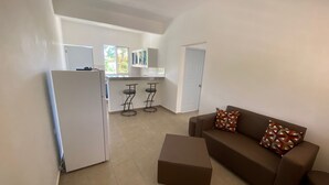 A modern apartment with a kitchen, a living area with a sofa and ottoman, and a dining area with bar stools.