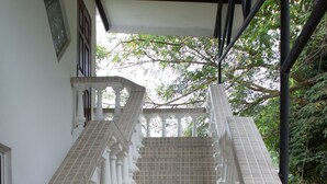 Una escalera con baldosas color crema y barandillas blancas que lleva a una zona cubierta con vista a árboles.