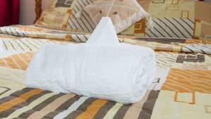 Una cama bien hecha con una toalla blanca, ropa de cama estampada y un cabecero de madera.