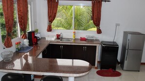 Una cocina con encimera de granito, dos taburetes, un fregadero, un refrigerador y una ventana con cortinas.