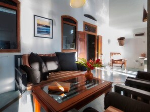 A modern living room with a sofa, a glass coffee table, and a wooden side table. There is a framed picture on the wall and a window with a view.