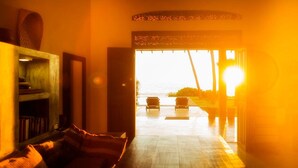 A cozy living room with a sofa, a bookshelf, and a view of the ocean at sunset. - Villananda by Interhome (Ambalangoda)