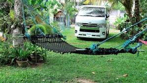 A white car parked in a lush garden with a hammock tied between trees. - Dominic's Home by Interhome (Weligama)