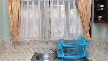 A kitchen with a sink, blue drying racks, and beige curtains with gold patterns.