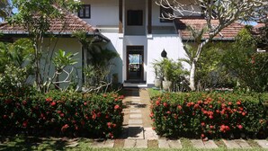 Ein zweistöckiges Haus mit Ziegeldach, einer zentralen Eingangstür und einem Garten mit roten Blumen.