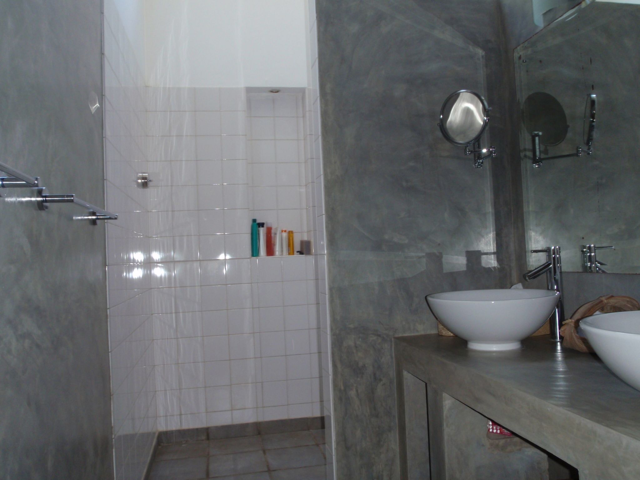 A bathroom with a white tiled shower area, a large mirror, and two sinks.