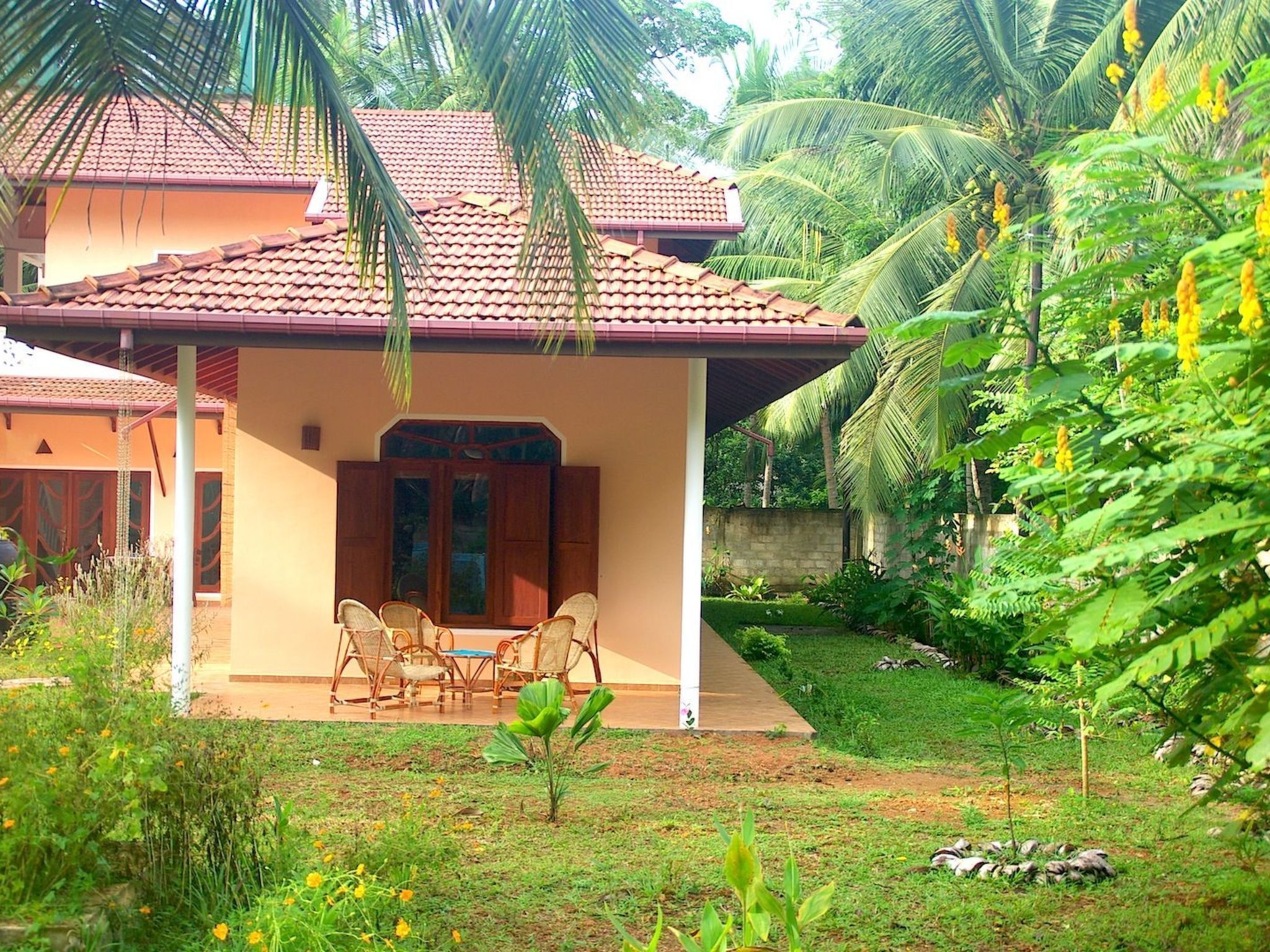 A house with a covered patio, a dining area with chairs, and lush greenery surrounding the property.