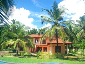 A two-story house with a red-tiled roof, surrounded by lush greenery and palm trees. - Dolphin by Interhome (Habaraduwa /Galle)