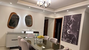 A dining area with a glass table, six chairs, a chandelier, and a large abstract painting on the wall. - Wohnung "Zayed Continental G" by Interhome (Cairo)