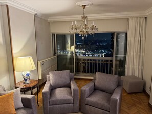 A modern hotel room with a large window offering a city view at night, a chandelier, and two grey armchairs. - Fenster der Wohnung mit Blick auf den Nil in Kairo by Interhome (Cairo)