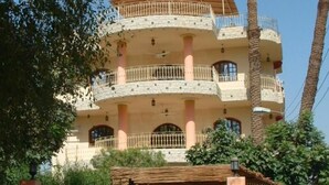 A multi-story residential building with balconies, a gated entrance, and palm trees in the background.