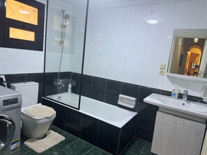 A modern bathroom with a glass-enclosed shower, a toilet, a washing machine, and a sink with a mirror. - "Classic Style apart". by Interhome (Abu Al Feda)