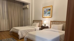 Ein Hotelzimmer mit zwei Betten, Holzboden, Teppich mit Muster, einem Bild an der Wand und einer Klimaanlage.