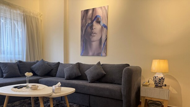 A modern living room with a grey sofa, a round coffee table, a small side table with a lamp, and a painting on the wall. - "Gemütliche 1-Zimmer-Wohnung". by Interhome (Abu Al Feda)