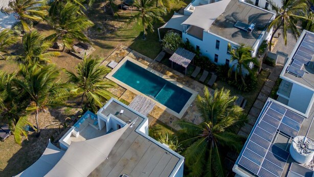 Luftaufnahme eines Küstenresorts mit mehreren Gebäuden, einem Schwimmbad und Palmen.