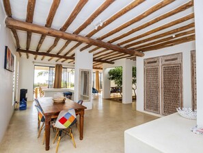 Amplia habitación con techo de madera, zona de comedor con mesa y sillas, y un gran ventanal con vistas al exterior.