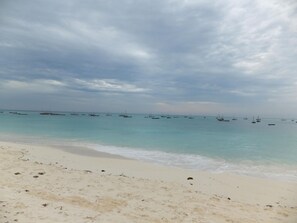 A beach with calm waters and several boats anchored in the distance.