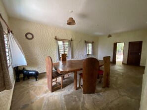 A dining area with a wooden table and chairs, stone flooring, and a textured wall.