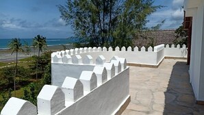 Ein weiß gekachelter Balkon mit Steinboden, der auf einen Strand und das Meer blickt.