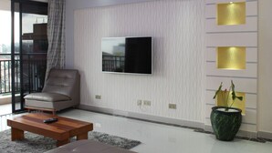 Un salon moderne avec un téléviseur à écran plat fixé au mur, un fauteuil en cuir, une table basse en bois et une plante en pot.