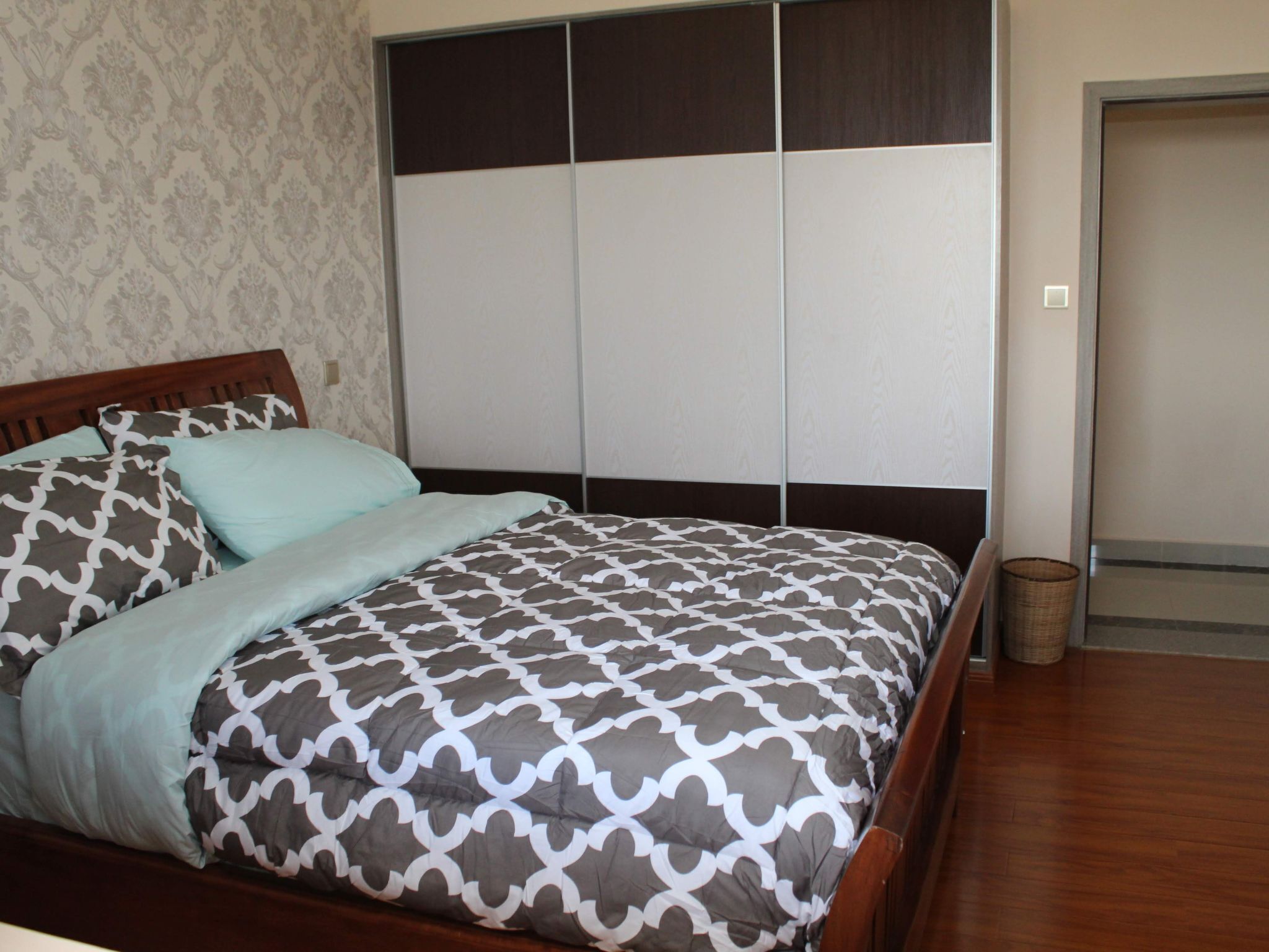 Un dormitorio con cama de madera, ropa de cama estampada, un armario con puertas correderas y un pequeño cubo de basura.