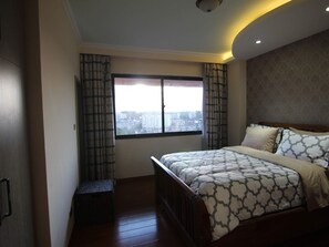 Ein Schlafzimmer mit einem großen Bett, Blick auf die Stadt durch ein Fenster und eine kleine Bank am Fenster.