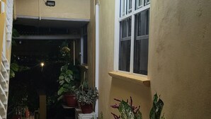 Ein schmaler Korridor mit Fliesenboden, Blumentöpfen und einem Fenster auf der rechten Seite.