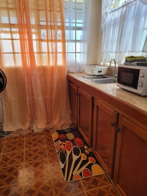 Cocina equipada con microondas, lavamanos y ventana con cortinas translúcidas.
