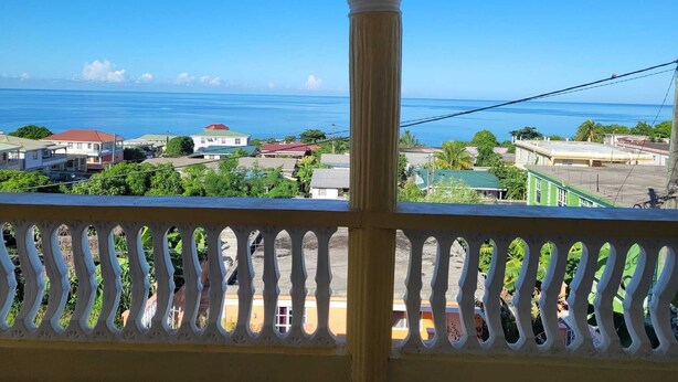 Ein Balkon mit Blick auf eine Küstenstadt, strahlend blauer Himmel und das Meer.