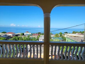 Ein Balkon mit Blick auf eine Küstenstadt, strahlend blauer Himmel und das Meer.